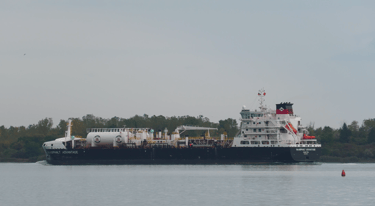 A blue and white tanker ship passing a red buoy with green trees in the background.
