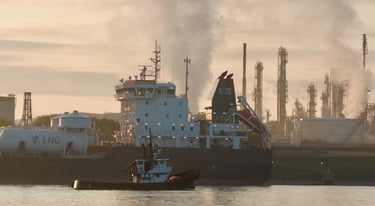 A tugboat passes by the aft section of a tanker ship moored at a refinery.