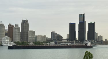 A huge freighter passing downtown Detroit buildings.