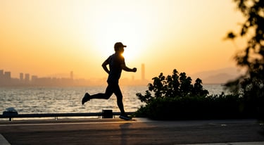 Silhouette of a man jogging along a coastal path during a golden sunrise with a city skyline in the background.