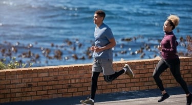 A man and woman jogging together along a scenic coastal road for outdoor fitness.