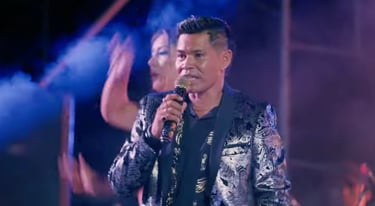 Roger Bardales  in a silver paisley suit performing live on stage singing Cumbia Masha..