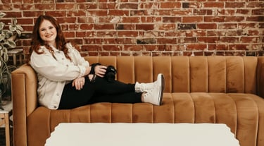 Rachel sits on a couch smiling at the camera