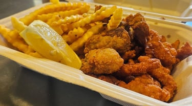 Fried oysters with fried clams, crinkle-cut fries and a lemon wedge in a takeout container from Captain’s Galley