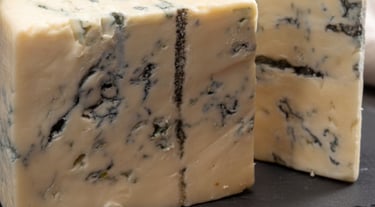 Two thick wedges of creamy blue cheese with blue-green veins on a black slate serving board.