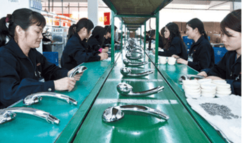 Factory workers assembling chrome shower heads on a green production line conveyor belt.