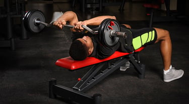 A man performing a lying triceps extension skull crusher exercise using an EZ curl bar on a weight bench.