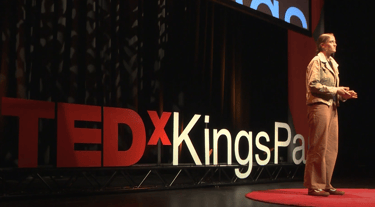 a woman standing on a stage making a TEDx speech