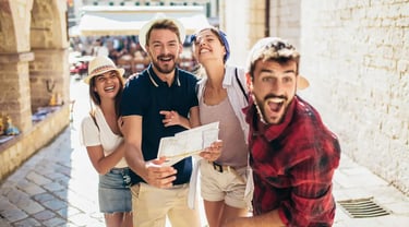 Cheerful group of young tourists laughing while exploring a sunlit European city street with a paper map.