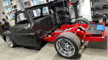 Custom black classic pickup truck restoration featuring a bright red chassis and chrome wheels in a garage.
