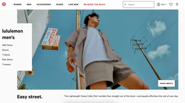 A from-below photograph of a man wearing a beige collared shirt, white t-shirt, and beige shorts.