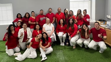 A diverse group of coworkers in red shirts and white pants pose for a team photo on green turf.