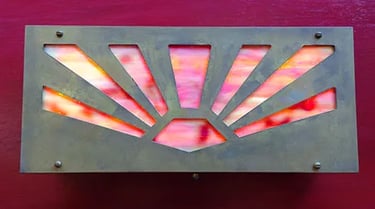 Brass sconce with colorful glass behind sunbust cutout.