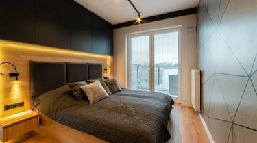 Nowoczesna sypialnia z łóżkiem, ciemnym zagłówkiem, drewnianą podłogą i oknem z żaluzjami