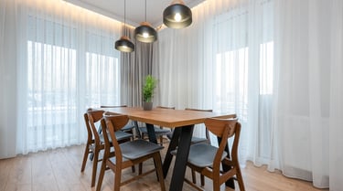 Drewniany stół z sześcioma krzesłami w jasnej jadalni z dużymi oknami i lampami