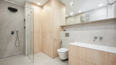 Nowoczesna łazienka z kabiną prysznicową, wiszącą toaletą, szafkami z jasnego drewna.