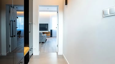 Nowoczesny korytarz z jasnymi płytkami, czarną zabudową i kinkietami na ścianie.