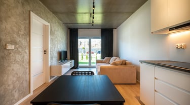 Salon z aneksem kuchennym: stół, sofa, telewizor oraz drzwi balkonowe.