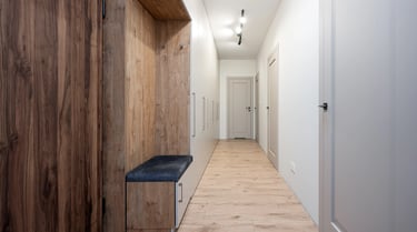 Wąski korytarz z zabudowaną szafą i siedziskiem, białe drzwi, drewniana podłoga