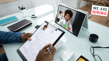 a person sitting at a desk with a tablet conducting an online job video interview with a guest
