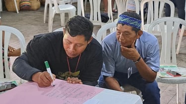 Two indigenous men in a workshop collaborating and writing on a pink poster at a community meeting.