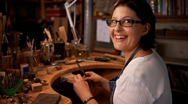 Una joyera artesana sonriente trabajando en un banco de trabajo de madera con herramientas profesion