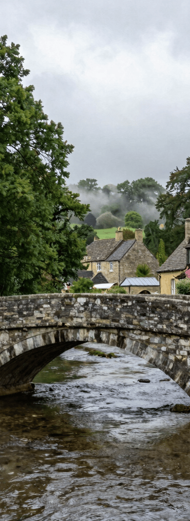 A traditional stone bridge over a clear river in a village like Burnsall. Green trees overhanging the water and mist white clouds above. A peaceful Northern European / British / Yorkshire scene.