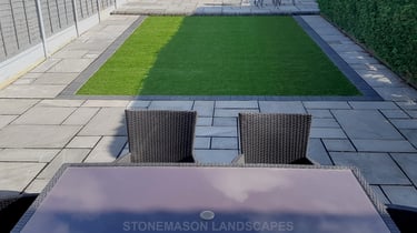 Fully paved grey sandstone patio with charcoal edging bocks and artificial grass lawn