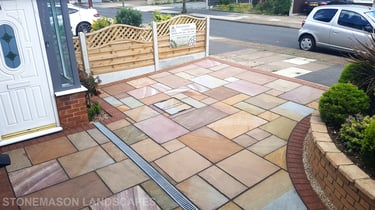 Colourful sandstone paving driveway and curved raised planter with colourful plants and flowers
