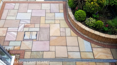 Colourful sandstone paving driveway and curved raised planter with colourful plants and flowers