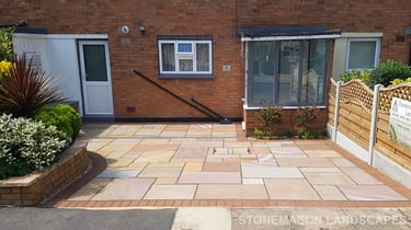 Colourful sandstone paving driveway and curved raised planter with colourful plants and flowers