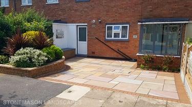 Colourful sandstone paving driveway and curved raised planter with colourful plants and flowers