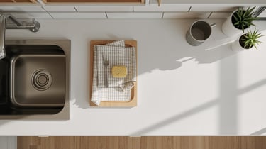 Top view of a clean white kitchen countertop with a stainless steel sink, wooden tray, and potted plants.