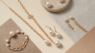 Elegant gold chain jewelry set featuring a pearl necklace, matching earrings, and a bracelet on a neutral background.