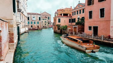 Um táxi aquático de madeira percorre um canal turquesa em Veneza, Itália, cercado por edifícios hist