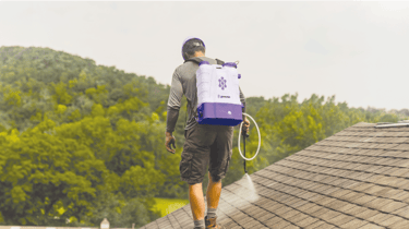 A professional roof cleaner uses a purple backpack sprayer to apply Go Nano to shingles.