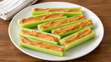 Fresh green celery sticks filled with creamy peanut butter served on a white plate as a healthy snack.