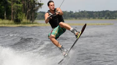 A man performing a jump on a wakeboard across a lake during a water sports session.