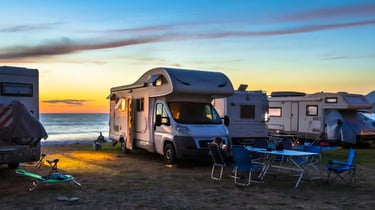 Motorhomes and camper vans parked at a beach campsite during a vibrant sunset over the ocean.