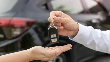 A person handing over electronic car keys to a new owner in front of a black vehicle.