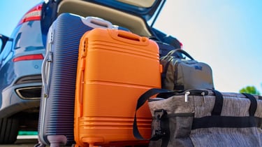 Suitcases and travel bags packed behind a car trunk for a family road trip.