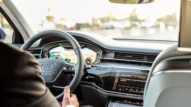 Driver sitting inside a modern Audi luxury sedan featuring a digital cockpit and leather interior.