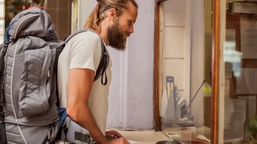 Bearded male traveler with a large backpack buying tickets at a station counter.