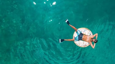 Aerial view of a man relaxing on a donut floatie in clear turquoise tropical ocean water.