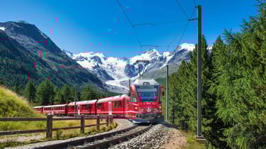 Red Bernina Express train traveling through the Swiss Alps with snowy mountain peaks and a glacier.