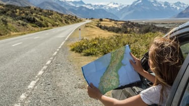 A person looks at a map during a scenic road trip with snow-capped mountains in the background.