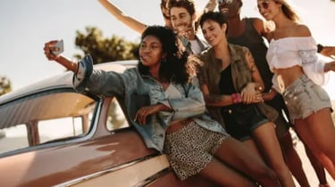 A diverse group of happy friends taking a selfie while leaning against a vintage car on a sunny road trip.