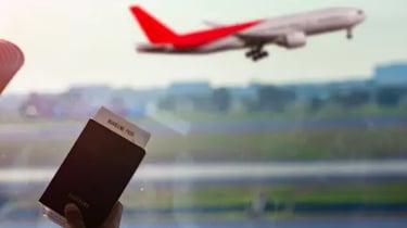 A traveler holding a passport and boarding pass at the airport as a plane takes off.
