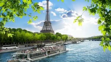 Eiffel Tower view from a Seine River cruise boat in Paris with green leaves in the foreground.