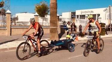Cyclist in a triathlon race pulling a child in a special needs bike trailer during a marathon event.